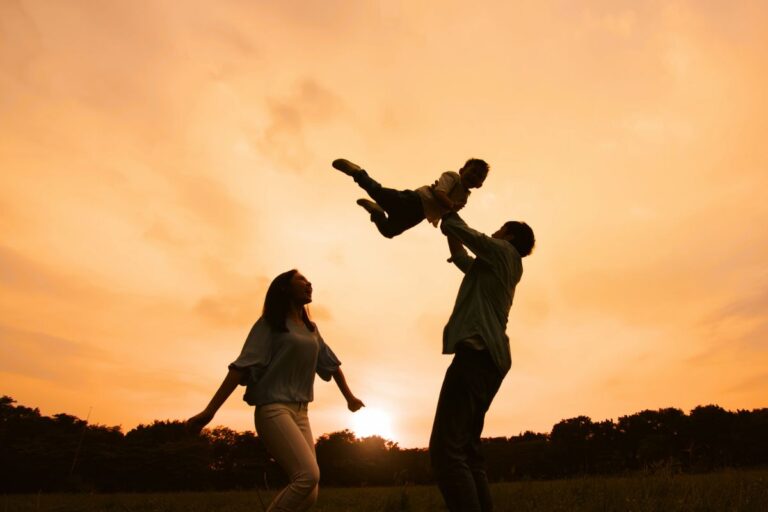 Famiglia al tramonto con papà che solleva bambino in aria mentre mamma guarda felice